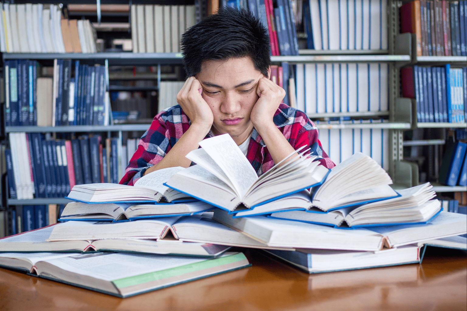College student frustrated looking down on a pile of books.