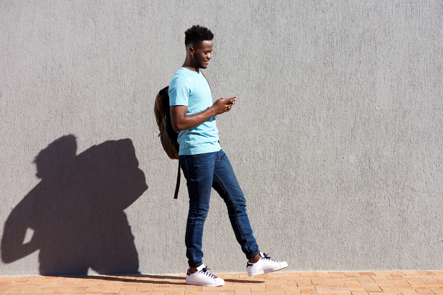 black student on mobile phone with shadow against wall